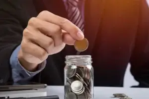Oseba daje kovanec v steklen kozarček, v katerem je že več kovancev.
